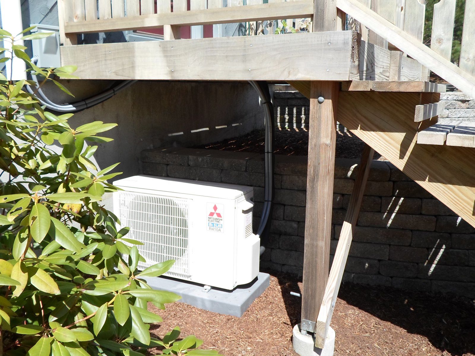 Mitsubishi heat pump outdoor unit tucked under a deck